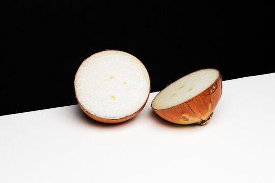 A round white onion with brown skin, freshly cut into two halves on the edge of a white table against a black background