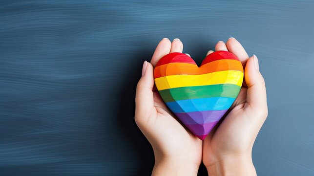 Woman hands holding LGBTQ rainbow community heart flag with rainbow colors isolated on blue background
