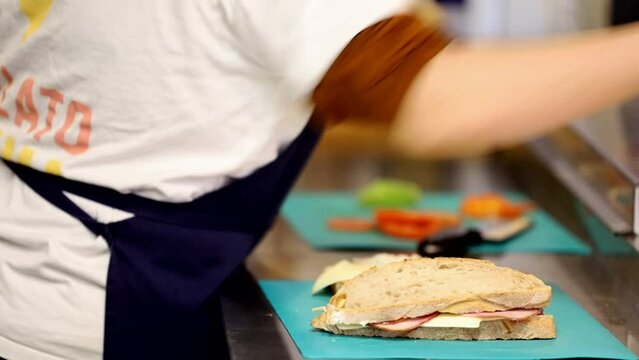 Stockholm, Sweden A male server in a cafe makes a sandwich on the stainless kitchen counter.