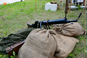 A close up on a machine gun replica from World War I seen next to some sandbags and ammo crates spotted next to a camp seen on a cloudy summer day during a historic reenactment in Poland