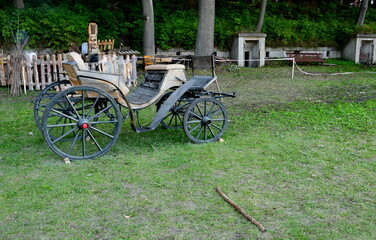 A close up on an old carriage or cart to be drawn by horses made out of wood and metal standing next to some wooden fence and concrete bunkers or bomb shelters seen in Poland in summer