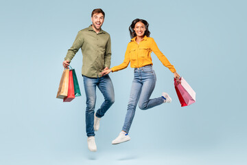 Joyful couple with shopping bags jumping, blue background