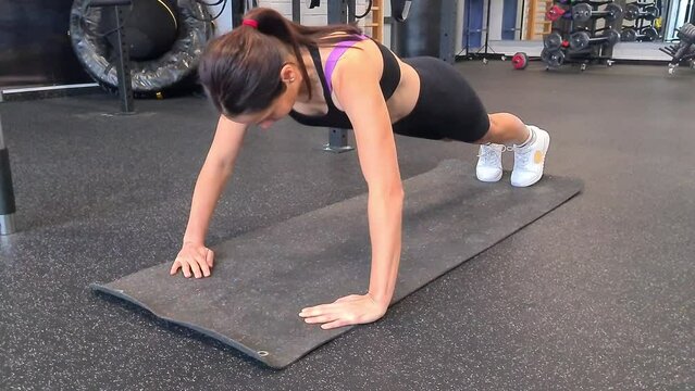 Young woman doing push-ups in gym. Healthy young woman working out on exercise mat