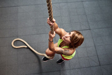 Focused on climbing rope sportswoman in gym.