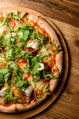Pizza with arugula and herbs on a round wooden stand on a table