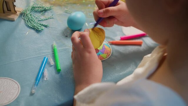 Little girl decorates Easter eggs with a marker, view from the back close-up