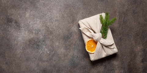 Christmas gift wrapped in fabric with a dried orange slice and a sprig of fir on a dark background....