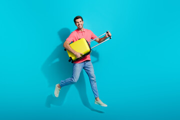 Fototapeta na wymiar Full length photo of excited cheerful guy dressed pink polo jumping high holding suitcase isolated blue color background