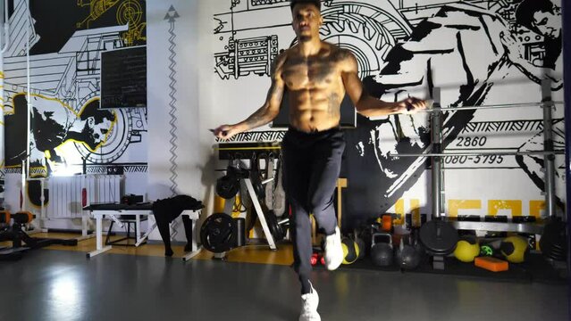 Muscular afro american sportsman skipping with a jump rope at sport club. Strong african athlete with tattoos exercising at modern gym. Young black sporty man doing cardio in fitness centre. Close up