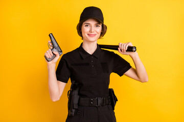 Photo of happy positive good mood policewoman in black uniform hold weapons isolated on yellow...