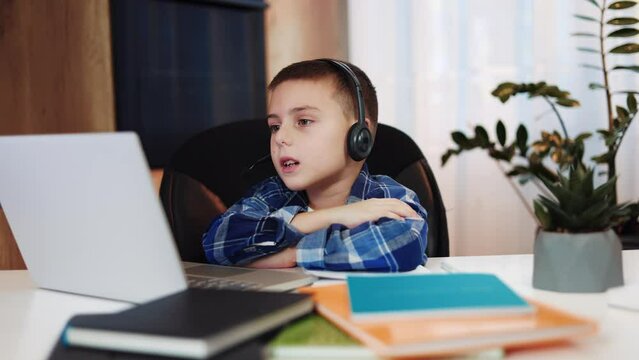Attentive caucasian boy with headset having video call with teacher on wireless laptop. Brainy male child engaging in extra classes in free time from school. Concept of education and technology.