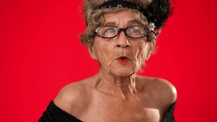 Closeup of funny elderly senior old woman with no teeth and wrinkled skin looks at camera has great idea gesture showing explosion of thinking posing isolated on red background