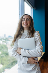 Female employee with dark hair in corporate business company. Businesswoman stands near wooden bench in company lounge zone