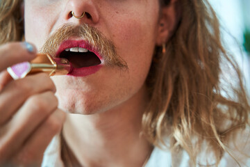 Cropped view of longhaired man with moustache holding lipstick and painting lips