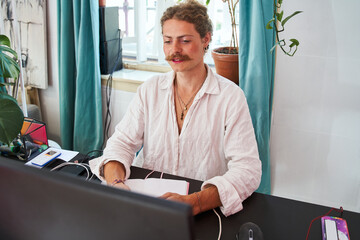 Satisfied young freelancer with face makeup sitting in office and working computer