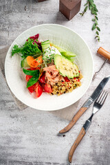 Salad with canned tuna, avocado and bulgur in a white plate. Served on a gray concrete table, top view