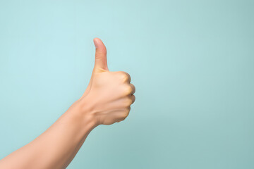 Close up of hand showing thumbs up sign in front of mint green background