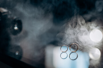 Two golden wedding rings with white smoke around, copy space and black background