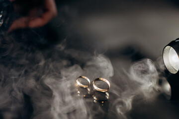 Two golden wedding rings with white smoke around, copy space and black background - obrazy, fototapety, plakaty