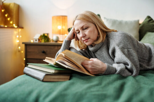 Мature woman reading book on bed at home. Christmas time, the magic of the holiday.