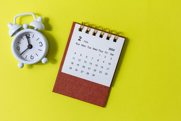 Fototapeta na wymiar Desk calendar for February 2024 and alarm clock on a yellow background with copy space.