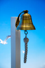 A sea bell or a rynda hanging on a wooden pole against a background of blue sky and seagulls. Ship...