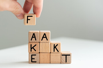 A man in a blue shirt composes the word FAKE from wooden cubes vertically