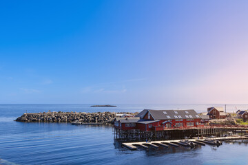Classic red Rorbu wooden houses and a dock in Moskenes, Lofoten Islands, Norway, gleaming under the...