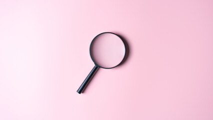Close up of a black magnifying glass on a pink background. Top view with copy space. Finding or...