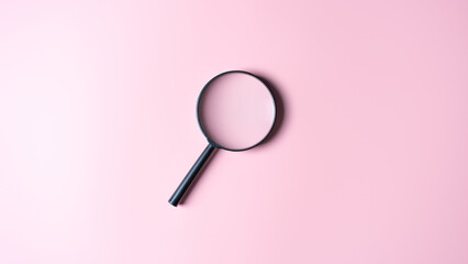 Close up of a black magnifying glass on a pink background. Top view with copy space. Finding or searching for ideas, explore for knowledge, find out. Magnifier finds answer. Science research concept.