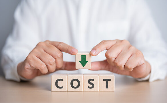 Businessman's hands hold wooden cube with a green arrow down and COST word. Lean optimize manufacturing. Decreasing company expense to maximize profits. Business process improvement to reduce cost.