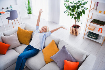 Photo portrait of attractive pensioner woman raise hands sit sofa enjoy weekend cheerful living...