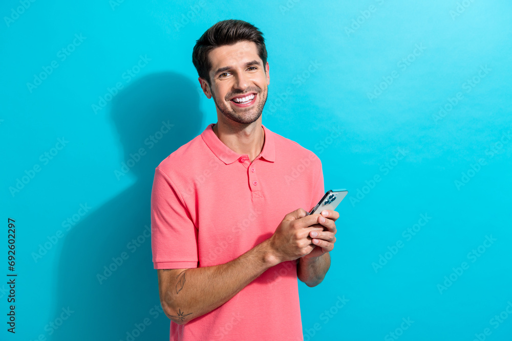 Poster Photo of cheerful young boyfriend sending a date request to girlfriend in application using phone isolated on cyan color background