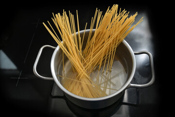 Spaghetti are boiled in a pot of water on a black stove top, cooking pasta, copy space, selected...