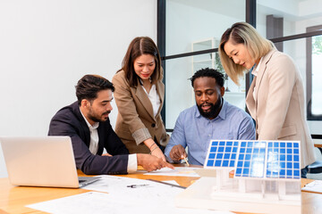 multiethnic coworkers discuss meeting on solar roof system project with solar panel house model,...