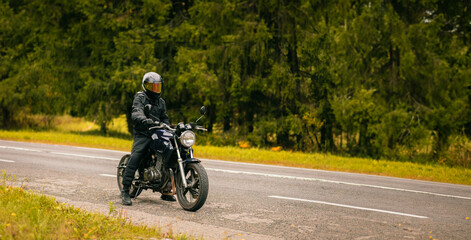 Obraz na płótnie Canvas motorcyclist in motorcycle clothing and a helmet on a custom stylish motorcycle on a forest asphalt road