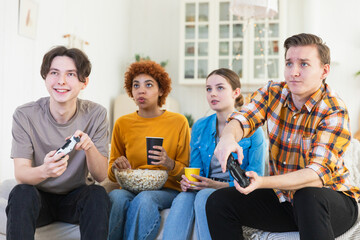 Home party. Cheerful group of friends playing video games at home. Happy diverse group buddies having fun together indoor. Friendship leisure entertainment concept. Young best friends enjoying weekend
