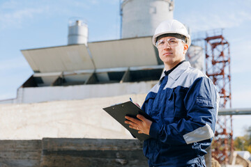 Civil engineer in uniform and helmet operates concrete plant and checks delivery on concrete mixer...