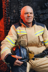 Happy officer fireman in uniform with helmet near wooden house after burning. Concept of saving lives, rescue service