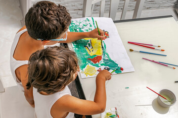 Two cute little brothers sitting at home, painting a horse in a meadow and trees with brushes on a...