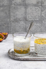 Chia pudding with passion fruit puree and yogurt in a glass on a grey background. Healthy vegetarian food. Tasty breakfast idea. Parfait with tropical fruit.