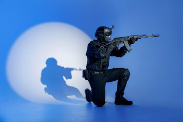 Action photo, Soldier in black uniforms with weapon standing on his knee in studio. Concept Military warrior army tactical force to fight crime in city