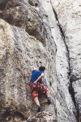 Young girl climber climbs a steep rock