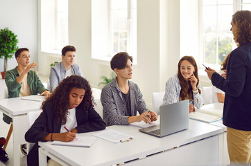 Obraz premium Teacher is talking and discussing topic with group of students while conducting lesson in college. Multiracial students sit at desks and answer questions from male teacher. Education concept.