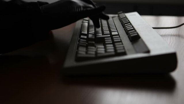 An unknown anonymous man in a black jacket and black gloves is typing a message on a computer keyboard. Video with sound.