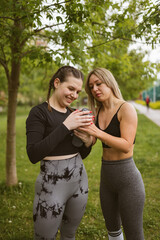 Young sportswomen hold water bottle standing in green city park. Slim athletes stay hydrated during...