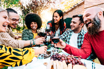 Multiracial people cheering red wine sitting outside at bar table - Group of friends having fun at...