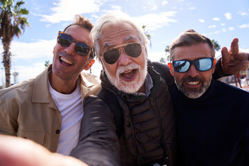Group of middle-aged Caucasian men wearing sunglasses taking a selfie with a cell phone, happy and smiling looking at camera enjoying their vacation outdoors on a sunny day. - Powered by Adobe