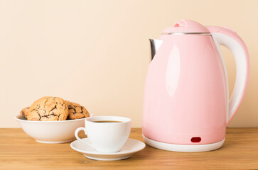 Pink electric kettle with cup of tea and dessert on table