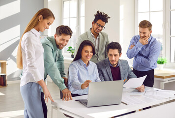 Team of business people using a modern computer during a work meeting in the office. Group of happy diverse men and women looking at the laptop on the desk - obrazy, fototapety, plakaty